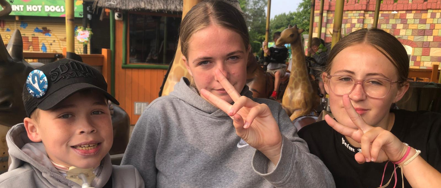 A boy with a tracheostomy sat with his two sisters