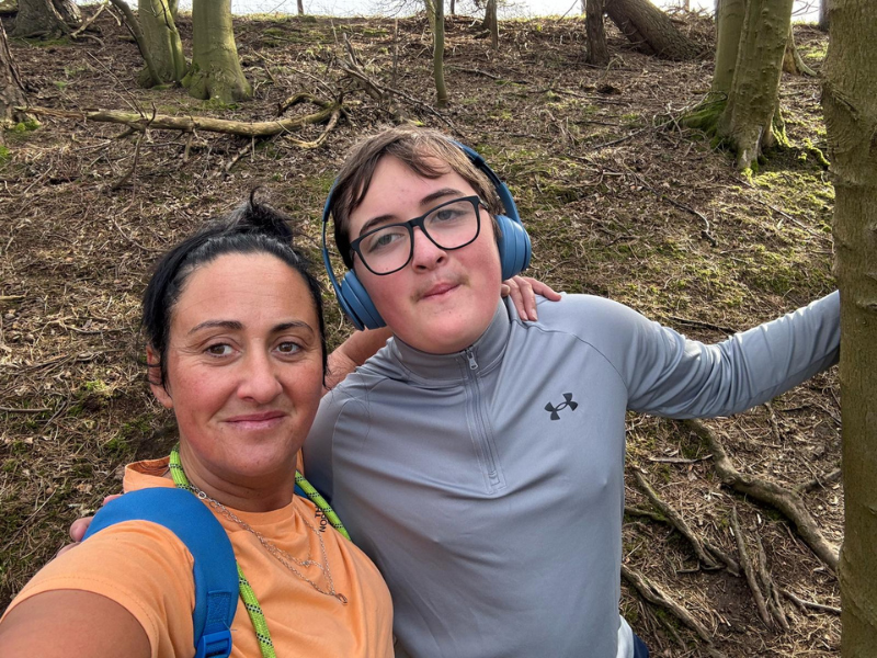 A woman and son with their arms around each other stood by a tree.