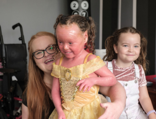 A young woman is sat next to her two daughters. They are all smiling.