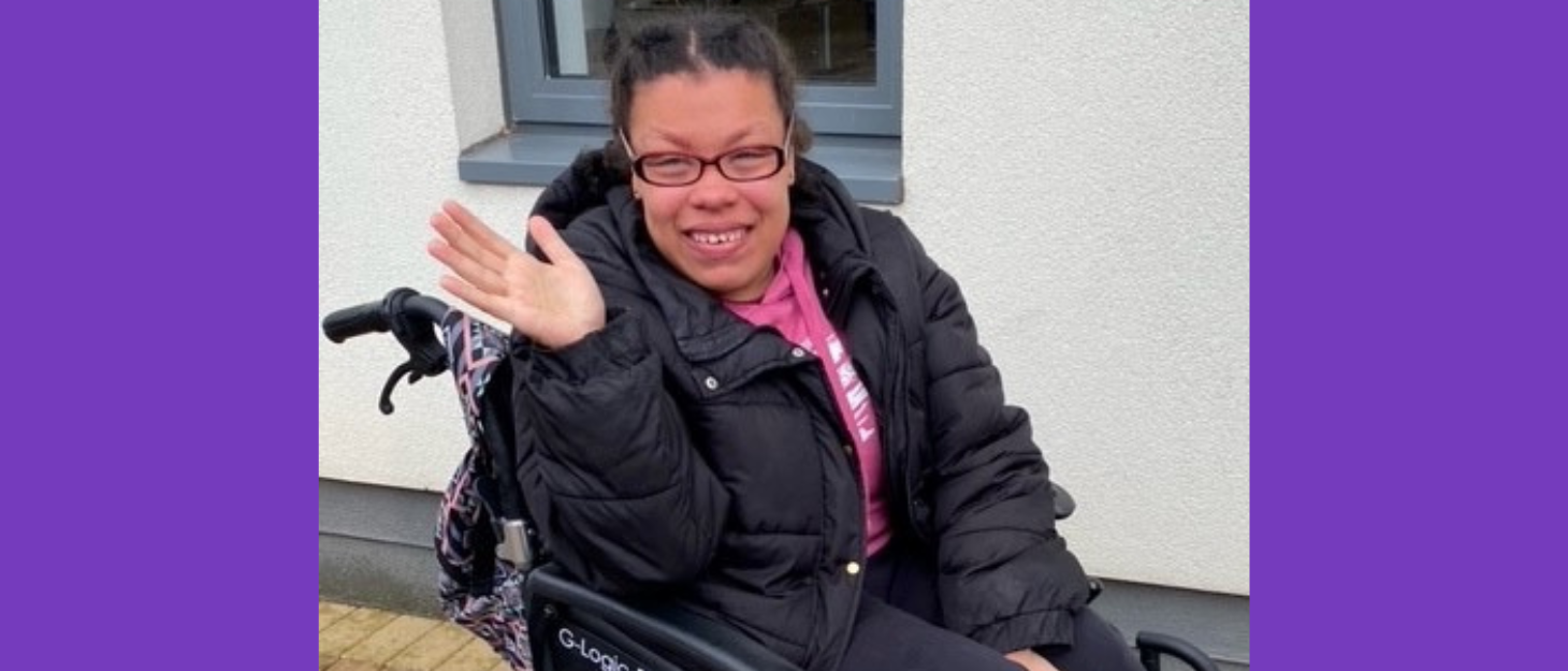 girl in wheelchair smiles and waves