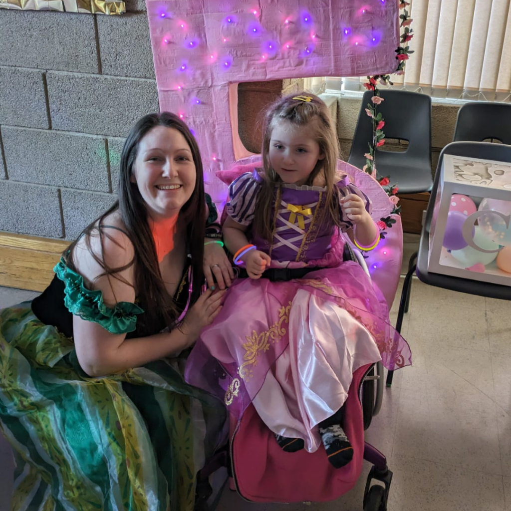 Charlotte is sat in her wheelchair next to her mum Jess posing for the camera.