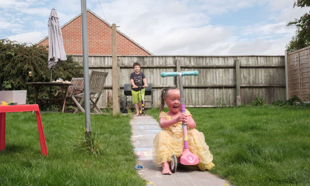 A girl on a scooter in her garden wearing a princess dress