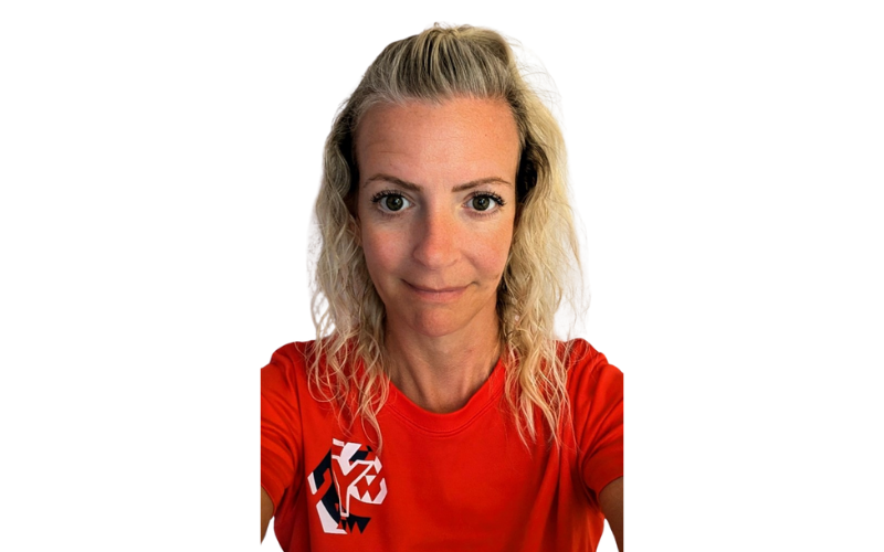 A woman with blonde wavy hair smiles, wearing a red top