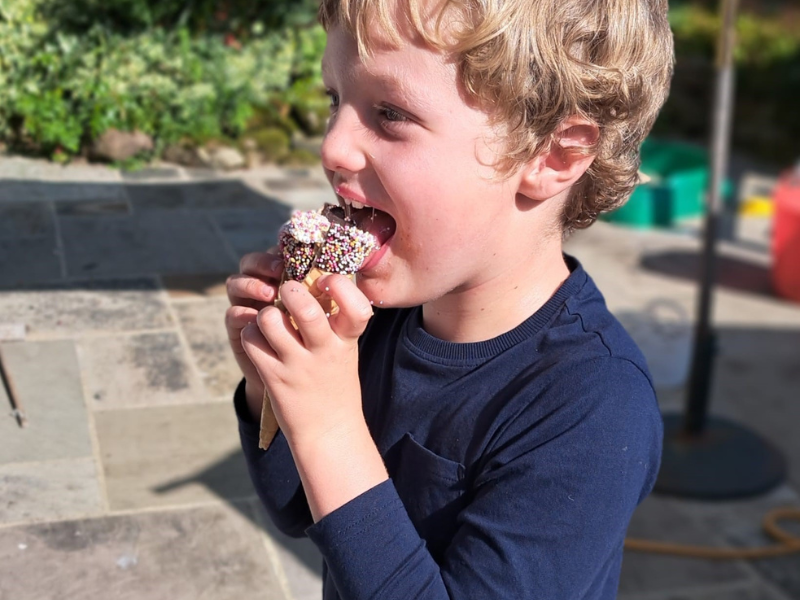 A little boy in a navy coloured top, sat outside eating an ice cream