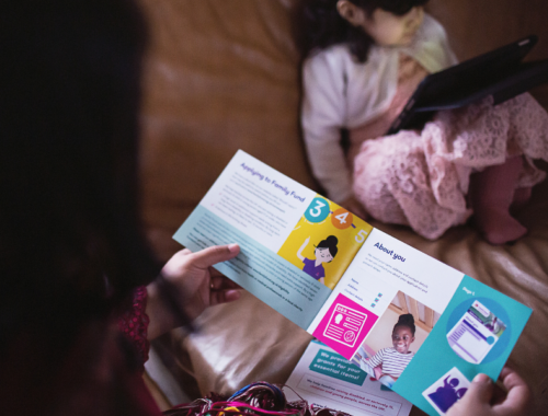 Someone looking at a Family Fund information leaflet. In the background is a child using a tablet