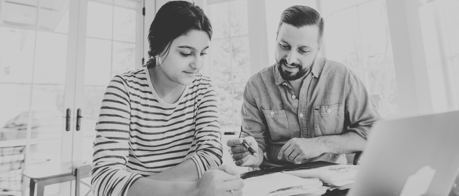 A man and woman looking at a laptop and making notes in grayscale