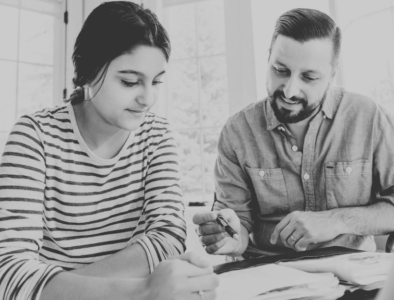 A man and woman looking at a laptop and making notes in grayscale