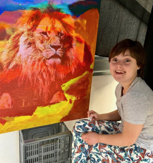 Charlotte is sat next to a painting of a lion and is smiling at the camera.