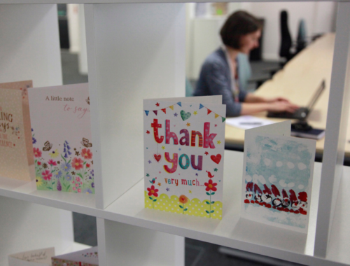 Thank you cards arranged on white shelves. In the background, a woman works on a laptop