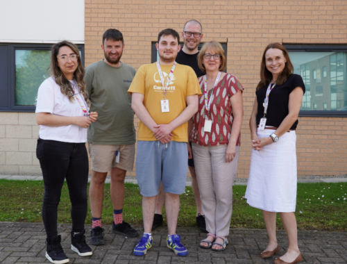 A photo of five Family Fund members of staff next to supported intern Tom smiling at the camera. They are standing outside Family Fund office building.