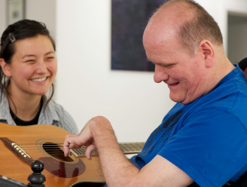A woman helps a disabled man with a guitar