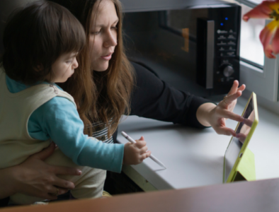 A mum is checking something on her iPad. She holds her young son in one arm