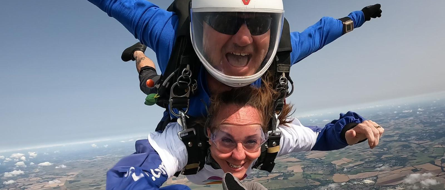 A tandem skydive in mid air, the man and woman both have their arms out smiling