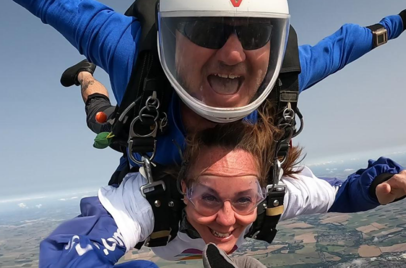 A tandem skydive in mid air, the man and woman both have their arms out smiling