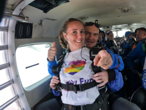 A tandem skydive with the man and woman sat in a plane before jumping. The woman is wearing a white Family Fund t-shirt smiling.
