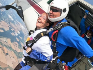 A tandem skydive as the man and woman lap from the plane. The woman is wearing a white Family Fund t-shirt smiling.