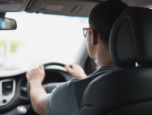 A young man wearing glasses driving a car