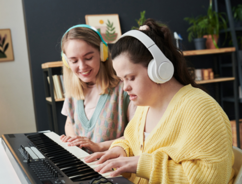Two young women are wearing headphones and are playing an electric keyboard.